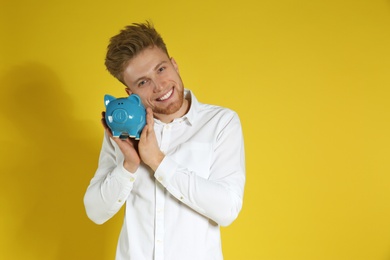 Young man with piggy bank on color background, space for text. Money saving