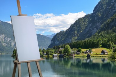 Wooden easel with blank canvas on table and beautiful mountain landscape. Space for text