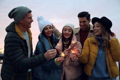 Group of people in warm clothes holding burning sparklers outdoors