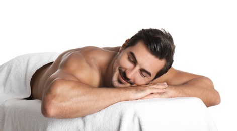Handsome young man relaxing on massage table against white background. Spa salon