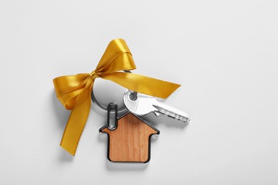 Photo of Key with trinket in shape of house and yellow bow on light grey background, top view. Housewarming party
