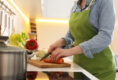 Woman cutting carrot to make bouillon in kitchen, closeup. Homemade recipe