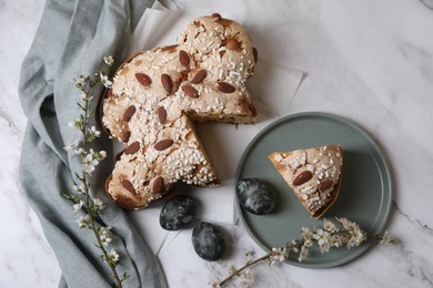 Photo of Delicious Italian Easter dove cake (traditional Colomba di Pasqua), painted eggs and branches with beautiful flowers on white marble table, flat lay
