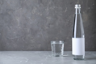 Bottle and glass with water on grey marble table, space for text