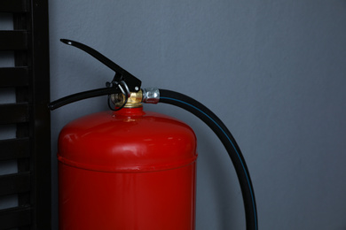 Fire extinguisher near grey wall indoors, closeup. Space for text