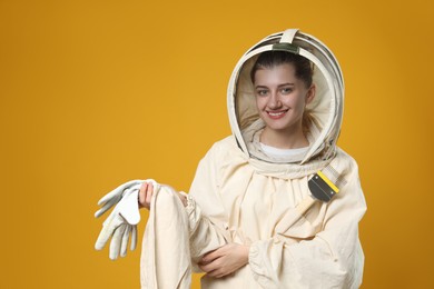 Photo of Beekeeper in uniform with gloves and uncapping fork on yellow background