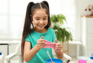 Cute little girl making DIY slime toy at table indoors