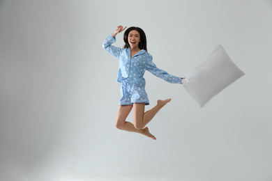 Beautiful Asian woman with pillow jumping on light grey background. Bedtime
