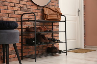 Rack with different shoes near red brick wall in hallway