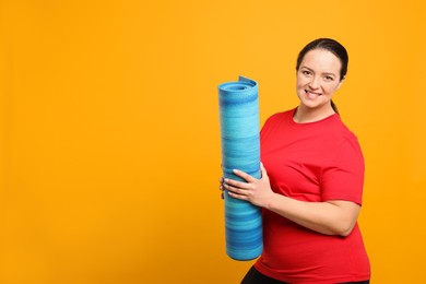 Happy overweight woman with yoga mat on orange background, space for text