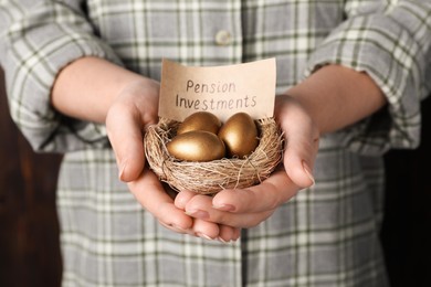 Woman holding golden eggs and card with phrase Pension Investments in nest, closeup