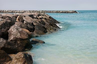 Picturesque view of beautiful rocky beach with breakwater on sunny day