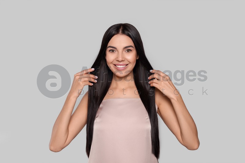 Portrait of beautiful young woman with healthy strong hair on light grey background