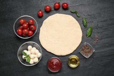 Raw dough and other ingredients for pizza on black table, flat lay