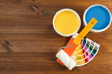 Buckets of paints, palette and roller on wooden background, flat lay. Space for text