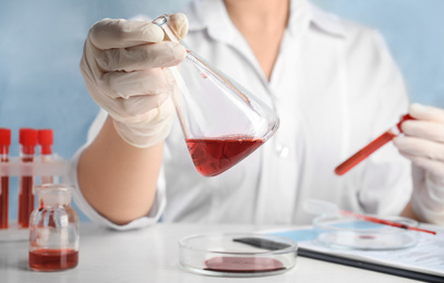 Scientist holding conical flask and tube with blood samples at table, closeup. Virus research