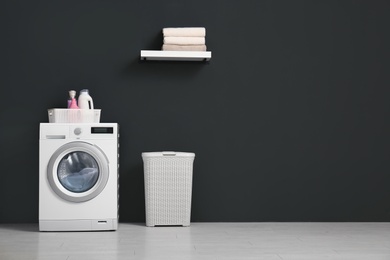 Modern washing machine, laundry basket and shelf with towels in bathroom. Space for text