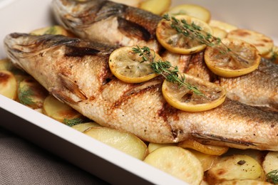 Photo of Baking tray with delicious roasted sea bass fish and potatoes, closeup