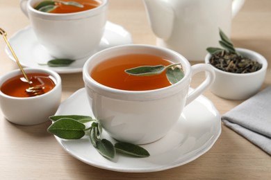 Cup of aromatic sage tea served with honey on wooden table