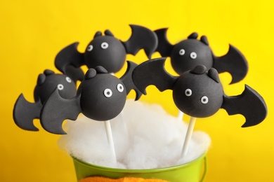 Delicious bat shaped cake pops on yellow background, closeup. Halloween treat