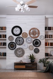 Stylish room interior with console table, beautiful houseplants and collection of different clocks on white wall