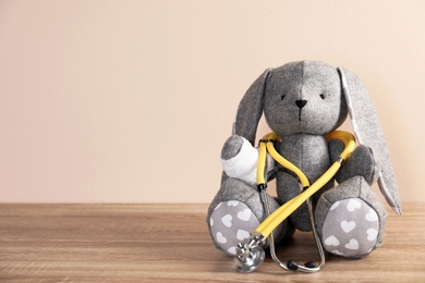 Photo of Toy bunny with stethoscope on table against color background, space for text. Children's hospital