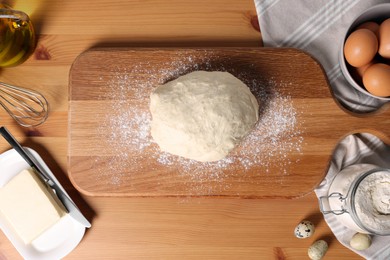 Photo of Fresh dough sprinkled with flour and other ingredients on wooden table, flat lay