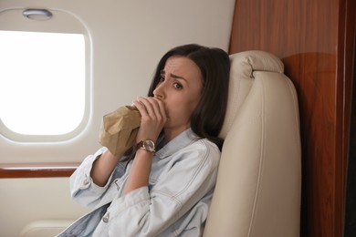 Nervous young woman with aviophobia breathing into paper bag in airplane
