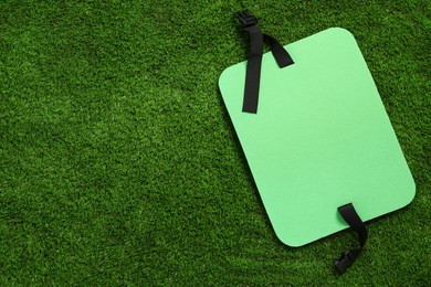 Bright foam tourist seat mat on green grass, top view. Space for text
