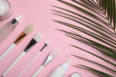 Different skin care products and brushes on pink background, flat lay