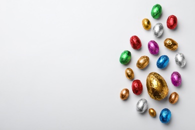 Chocolate eggs wrapped in colorful foil on white background, flat lay. Space for text