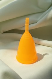 Menstrual cup on light fabric. Reusable female hygiene product