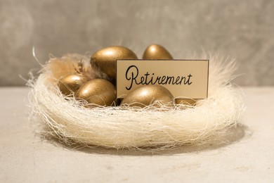 Golden eggs and card with word Retirement in nest on light table. Pension concept