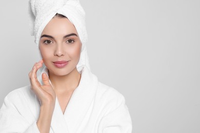 Photo of Young woman in bathrobe with towel on light grey background, space for text. Spa treatment