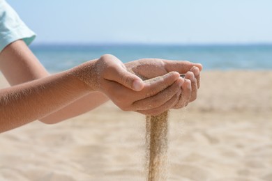 Child pouring sand from hands on beach near sea, closeup. Fleeting time concept