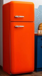 Photo of Modern closed refrigerator near colorful wall in kitchen. Domestic appliance
