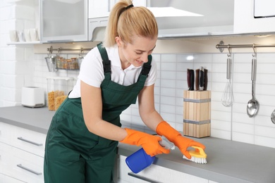 Female janitor cleaning kitchen counter with brush in house