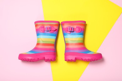Pair of striped rubber boots on color background, top view