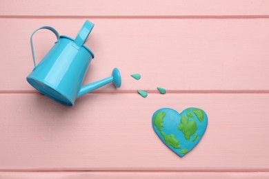 Happy Earth Day. Flat lay composition with heart shaped plasticine planet and watering can on pink wooden table