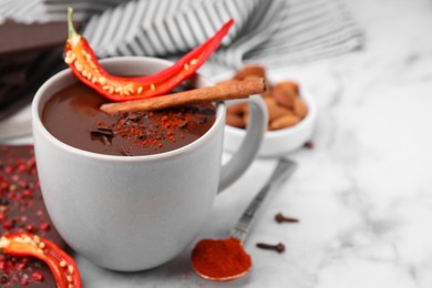 Photo of Cup of hot chocolate with chili pepper and cinnamon on white marble table, closeup. Space for text