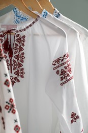 Beautiful shirts with different embroidery designs hanging on grey background, closeup. Ukrainian national clothes