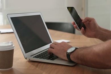 Freelancer working with laptop and smartphone at table indoors, closeup