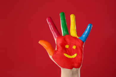 Kid with smiling face drawn on palm against red background, closeup