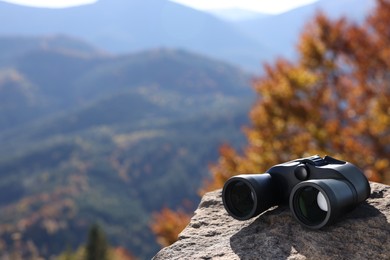 Modern binoculars on stone in mountains, space for text