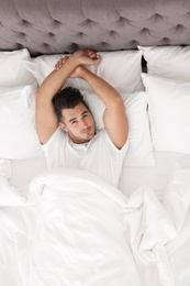 Photo of Young man lying in bed with soft pillows at home, top view