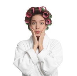 Emotional young woman in bathrobe with hair curlers on white background