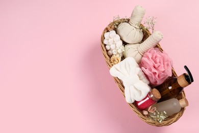 Spa gift set with different products in wicker basket on pink background, top view. Space for text