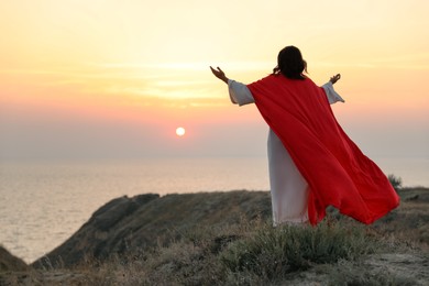 Jesus Christ raising hands on hills at sunset, back view. Space for text