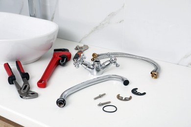 Parts of water tap and wrenches on white countertop in bathroom