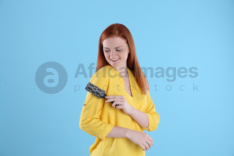 Photo of Young woman cleaning clothes with lint roller on light blue background